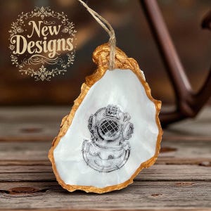 May include: An oyster shell decoration with a gold-painted edge and a white interior. It features a black and white illustration of a vintage diving helmet. The text "New Designs" is in the upper left corner.