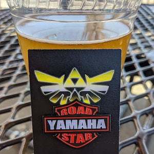 May include: A black and white enamel pin with a yellow and white triangular design and the text "ROAD YAMAHA STAR" in red, white, and black.