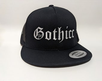 Puede incluir: Gorra de camionero negra con un "Gothic" bordado en blanco en letras antiguas.