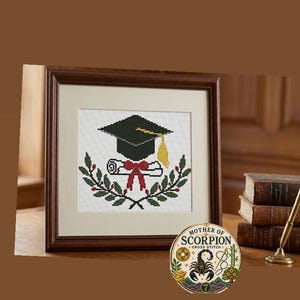 May include: A framed cross-stitch artwork featuring a black graduation cap with a yellow tassel, a white diploma tied with a red ribbon, and a green laurel wreath. A circular logo in the corner reads MOTHER OF SCORPION CROSS STITCH.