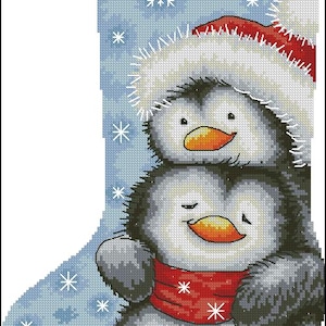May include: Christmas stocking featuring two penguins. The penguins are wearing a red scarf and a Santa hat. The background is light blue with snowflakes. The stocking has a red stripe at the top.