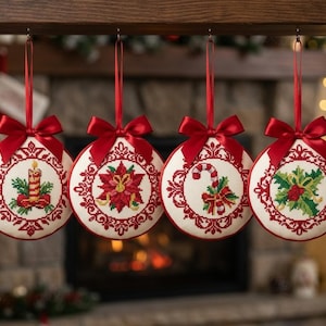 Könnte beinhalten: Vier runde, weiße Stoffornamente mit roten Kreuzstich-Stickmustern. Jedes Ornament zeigt ein einzigartiges Weihnachtsmotiv: eine Kerze, einen Weihnachtsstern, eine Zuckerstange und Stechpalmenblätter. Jedes ist mit einer roten Satinschleife verziert.