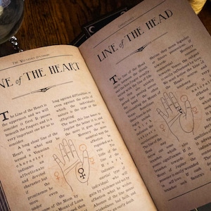 K&ouml;nnte beinhalten: Ein aufgeschlagenes Buch mit gealterten, sepiafarbenen Seiten, das schwarzen Text und Handfl&auml;chenillustrationen zeigt. Die linke Seite ist mit Line of the Heart und die rechte mit Line of the Head betitelt. Beide Seiten enthalten detaillierte Handlesediagramme.
