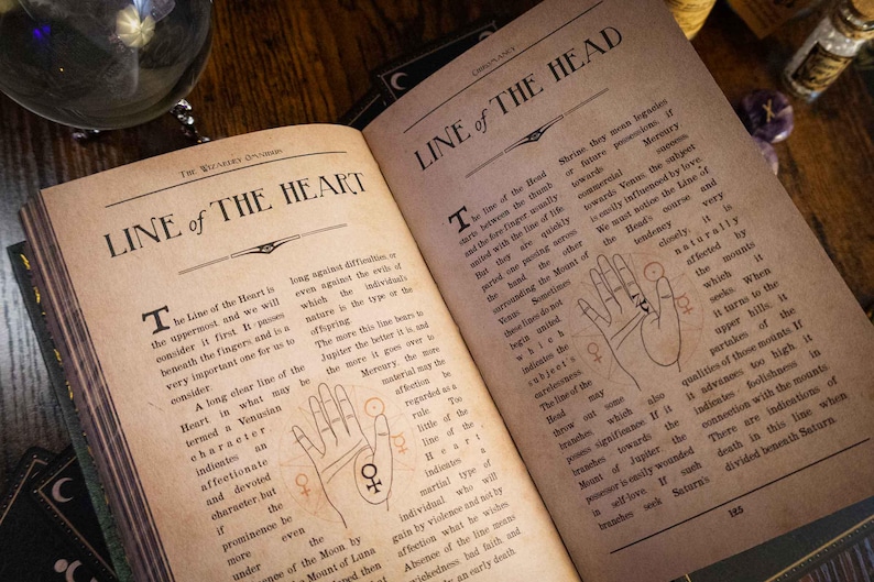 K&ouml;nnte beinhalten: Ein aufgeschlagenes Buch mit gealterten, sepiafarbenen Seiten, das schwarzen Text und Handfl&auml;chenillustrationen zeigt. Die linke Seite ist mit Line of the Heart und die rechte mit Line of the Head betitelt. Beide Seiten enthalten detaillierte Handlesediagramme.