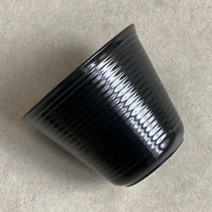 Könnte beinhalten: Ein schwarzer Keramiktopf mit einem strukturierten, gerippten Design. Der Topf ist leer und hat eine leicht abgerundete Form.