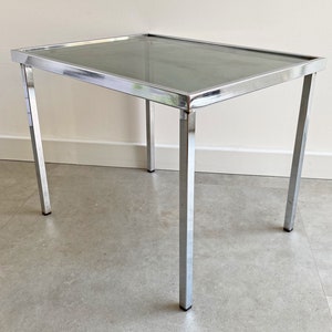 May include: A chrome-plated side table with a glass top. The table has a simple, modern design and is perfect for a small space.
