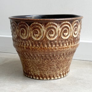 Może przedstawiać: Brązowa ceramiczna donica z teksturowaną powierzchnią i dekoracyjnym wzorem spiralnym na górze. Wnętrze jest ciemne, a donica ma rozkloszowany kształt. Przedmiot dekoracyjny do domu.