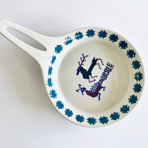 Pu&ograve; includere: Un piatto in ceramica bianca con un bordo blu e verde e un design di cervo stilizzato al centro.