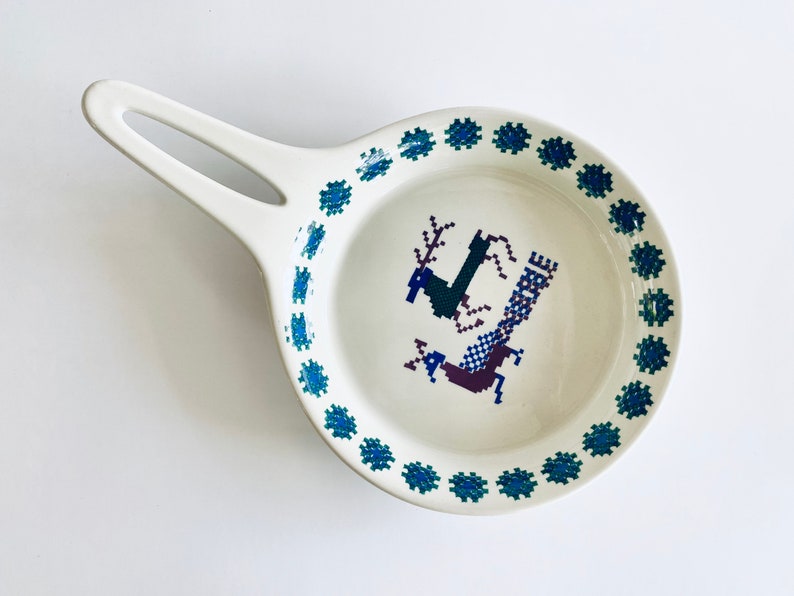 Pu&ograve; includere: Un piatto in ceramica bianca con un bordo blu e verde e un design di cervo stilizzato al centro.