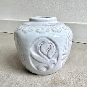 May include: A white ceramic vase with a round body and a narrow neck. The vase features embossed floral designs and a crackled glaze. The vase is approximately 6 inches tall and is suitable for displaying flowers or as a decorative item.