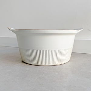Könnte beinhalten: Weißer Keramiktopf mit zwei Griffen und einem gerippten Design.