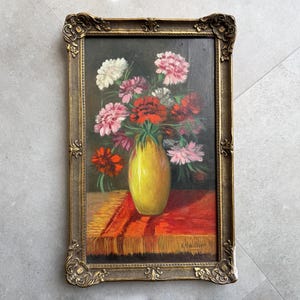 May include: A framed painting of a yellow vase filled with pink, red, and white flowers. The vase is sitting on a red and gold patterned tablecloth.
