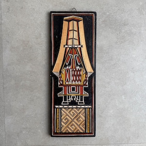 Könnte beinhalten: Ein rechteckiges Wandbild aus Holz mit schwarzem Hintergrund. Das Kunstwerk zeigt ein stilisiertes, symmetrisches Design in den Farbtönen Beige, Rot, Gelb und Weiß. Das Design ähnelt einer traditionellen Struktur oder einem Gebäude. Das Stück ist etwa 61 cm hoch.