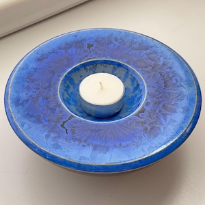 May include: A blue ceramic candle holder with a white tea light candle in the centre. The holder has a decorative design of blue and white swirls.