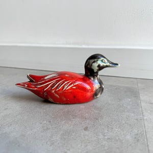 May include: A red and black ceramic duck figurine. The duck has a glossy red finish with black accents on the head and beak.