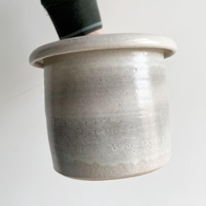 May include: A set of three ceramic mugs with a speckled, matte finish. The mugs are in shades of cream, light gray, and dark gray. Each mug has a simple, minimalist design and a rounded handle.