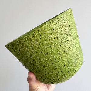 May include: A tapered, cylindrical plant pot with a vibrant lime green exterior. The surface features a heavy, rough, and granular texture that resembles coarse stone or bark, with a wide, open top and a narrower, flat base for stability.