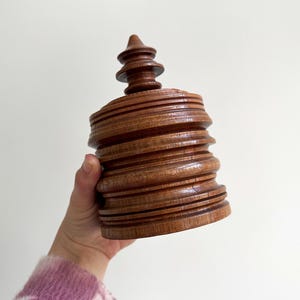 Pu&ograve; includere: Una scatola di legno con un design a spirale a pi&ugrave; livelli e una parte superiore appuntita. La scatola &egrave; realizzata in legno marrone scuro e ha una finitura liscia e lucida.