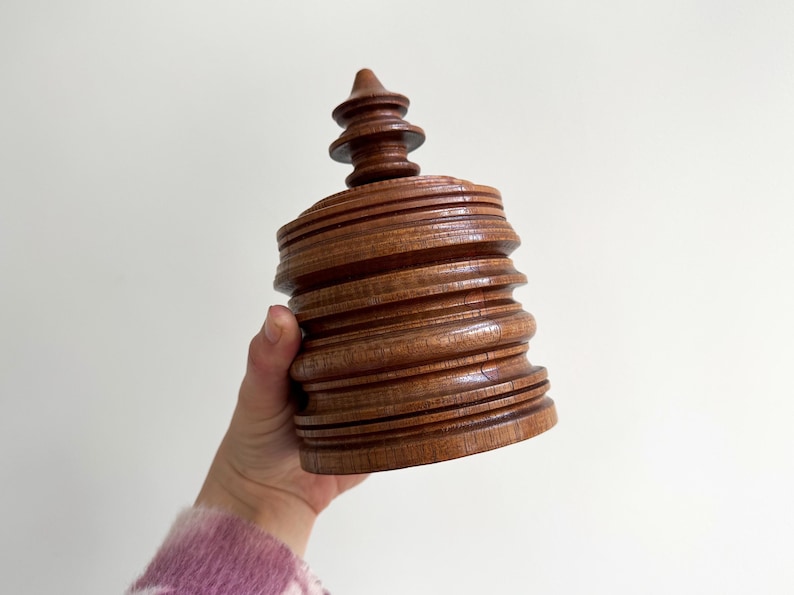 Pu&ograve; includere: Una scatola di legno con un design a spirale a pi&ugrave; livelli e una parte superiore appuntita. La scatola &egrave; realizzata in legno marrone scuro e ha una finitura liscia e lucida.