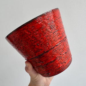 Peut inclure: Un pot en céramique rouge avec une surface texturée et striée. Le pot a une forme légèrement conique et un bord foncé. Le pot rouge vif avec des accents sombres est adapté à l'intérieur ou à l'extérieur.