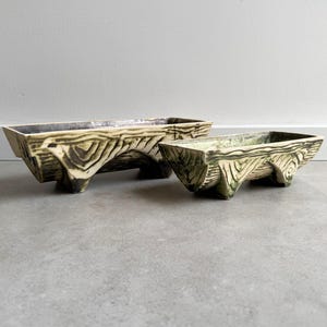 Peut inclure: Deux pots en céramique avec un motif géométrique vert et blanc. Les pots ont quatre pieds et sont de forme rectangulaire.