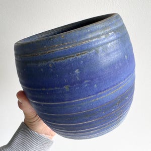 Pode incluir: Um vaso de cerâmica arredondado com um esmalte azul profundo e textura canelada horizontal. A superfície apresenta variações subtis de cor, com tons de azul escuro e acastanhados visíveis ao longo das cristas e do rebordo do vaso.