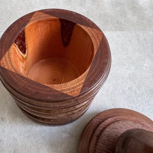 Pu&ograve; includere: Un set di mortaio e pestello in legno con un esterno marrone scuro e un interno marrone chiaro. Il mortaio &egrave; realizzato con pi&ugrave; strati di legno, creando un motivo unico.