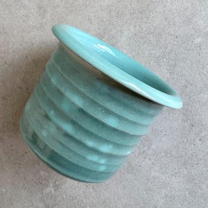 Op de afbeelding: Een lichtblauwe keramische plantenpot met een golvend, getextureerd ontwerp. De pot heeft een brede, afgeronde rand.