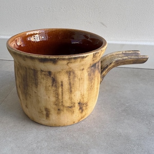 Puede incluir: Una olla de cerámica marrón y beige con una sola asa. La olla tiene un esmalte marrón en el interior y un esmalte moteado marrón y beige en el exterior.