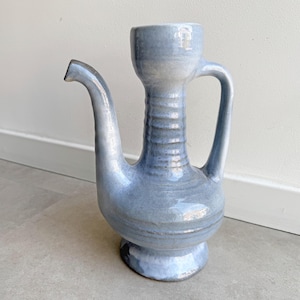 Könnte beinhalten: Hellblaue Keramikkrug mit langem Ausguss und Henkel. Der Krug hat einen bauchigen Boden und einen zylindrischen Hals. Die Gesamthöhe beträgt ca. 30 cm.