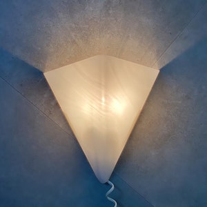 May include: A white triangular wall sconce with a frosted glass shade. The light is on and illuminates the room.