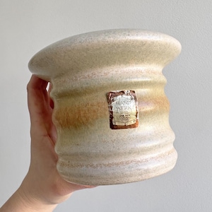 May include: A white ceramic mug with a black handle and the text "But First, Coffee" in a bold, black font. The mug is set against a blurred background, suggesting a cozy setting. The mug appears to be approximately 4 inches tall.