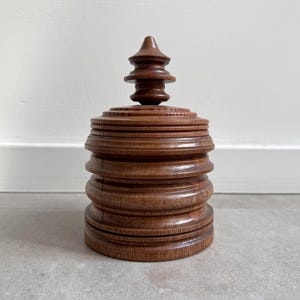 Pu&ograve; includere: Una scatola di legno con un design a strati e a gradini e una parte superiore appuntita. La scatola &egrave; realizzata in legno marrone scuro e ha una finitura liscia e lucida.