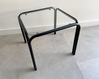 May include: A black metal side table with a glass top. The table has a simple, modern design.