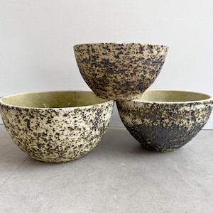 Puede incluir: Tres cuencos de cerámica con un esmalte moteado verde y negro. Los cuencos están apilados uno encima del otro.