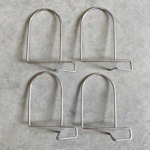 Puede incluir: Cuatro sujetalibros de metal plateado con un diseño simple y curvo. Cada sujetalibros tiene una parte superior redondeada y una base plana.