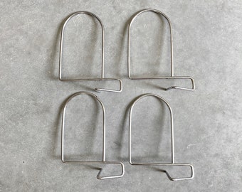 May include: Four silver metal bookends with a simple, curved design. Each bookend has a rounded top and a flat base.