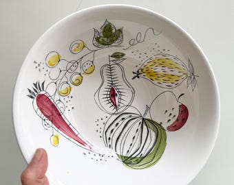 May include: White ceramic bowl with a hand-drawn fruit design. The bowl features illustrations of a red carrot, yellow grapes, a pear, a yellow fruit, a green and white striped fruit, and a red and white apple. Black outlines and green leaves complete the design.