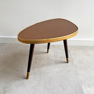 May include: A mid-century modern side table with a brown oval top and a gold trim. The table has three dark wood legs.