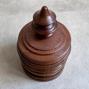 Pu&ograve; includere: Una scatola di legno marrone scuro con un coperchio a pi&ugrave; livelli e una parte superiore a punta. La scatola ha una finitura liscia e lucida.
