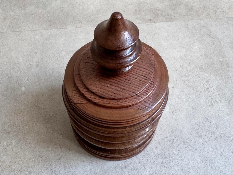 Pu&ograve; includere: Una scatola di legno marrone scuro con un coperchio a pi&ugrave; livelli e una parte superiore a punta. La scatola ha una finitura liscia e lucida.
