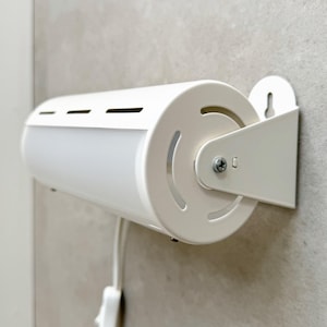 May include: A white cylindrical wall-mounted lamp featuring a frosted light panel, horizontal ventilation slots, and a metal bracket with a keyhole slot for mounting. The fixture includes a white power cord with an inline switch attached.