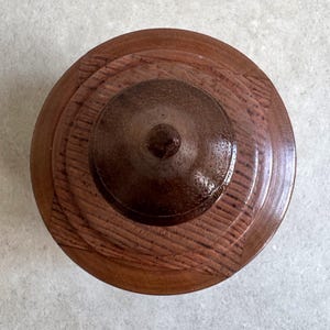Pu&ograve; includere: Un coperchio in legno con un centro marrone scuro e anelli concentrici di legno pi&ugrave; chiaro.