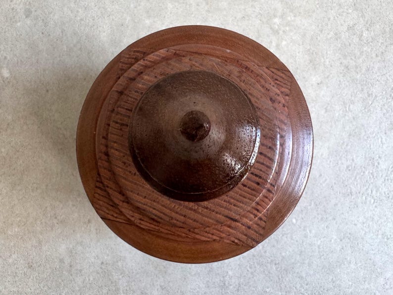Pu&ograve; includere: Un coperchio in legno con un centro marrone scuro e anelli concentrici di legno pi&ugrave; chiaro.