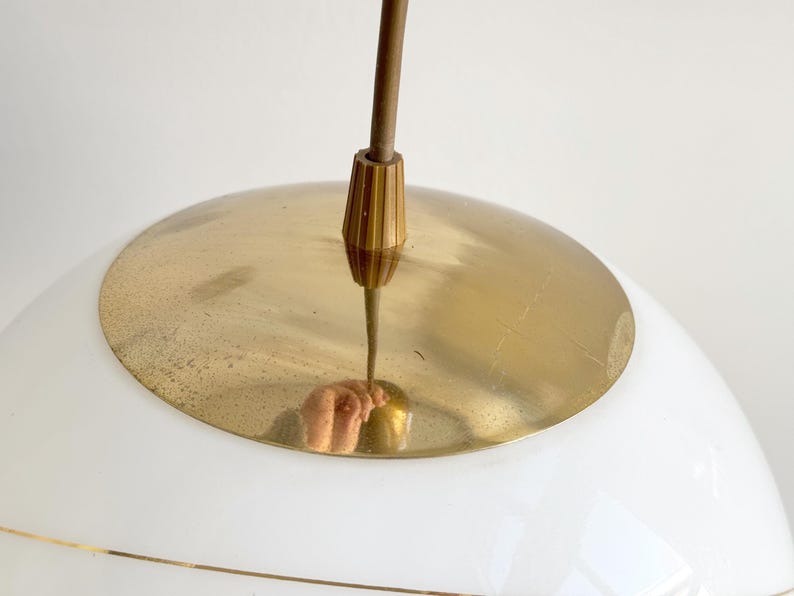Puede incluir: Una l&aacute;mpara colgante de globo blanco con una parte superior de metal dorado y una varilla de lat&oacute;n que cuelga del techo.
