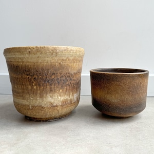 Könnte beinhalten: Zwei Keramik-Töpfe, einer groß und einer klein. Der größere Topf ist hellbraun mit einer dunkelbraunen Glasur. Der kleinere Topf ist dunkelbraun mit einer hellbraunen Glasur.