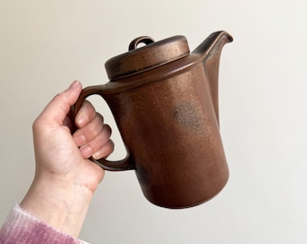 Puede incluir: Una cafetera de cerámica marrón con tapa y asa. La cafetera tiene una textura moteada.