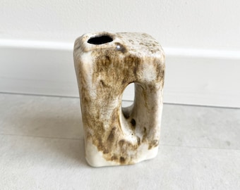 May include: A white ceramic vase with brown glaze, featuring a unique cutout design. The vase has a square base and a rounded top with a small opening for flowers.