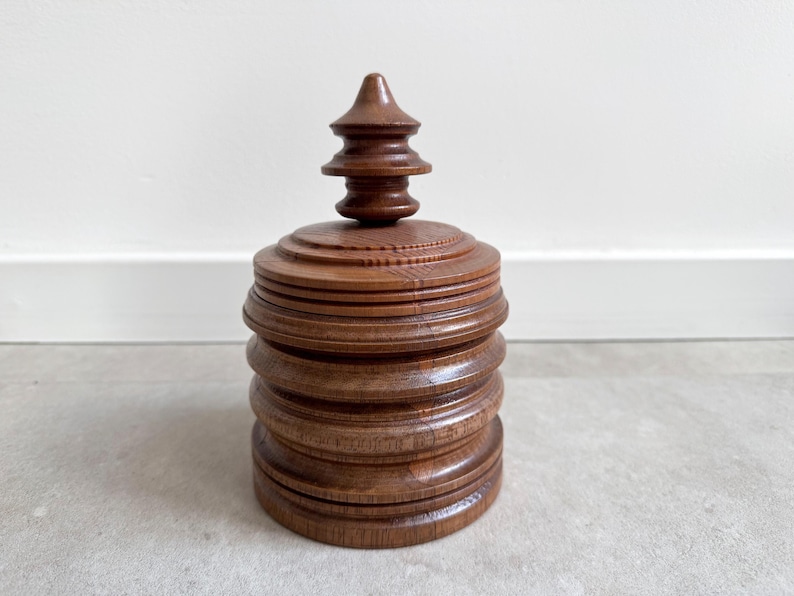 Pu&ograve; includere: Una scatola di legno con un design a strati e a gradini. La scatola ha una finitura marrone scuro e un coperchio appuntito a pi&ugrave; livelli.