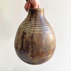 Puede incluir: Una taza de cerámica blanca con un asa negra y el texto "But First, Coffee" en negrita negra. La taza está llena de un líquido oscuro, probablemente café, y se encuentra sobre una superficie clara.